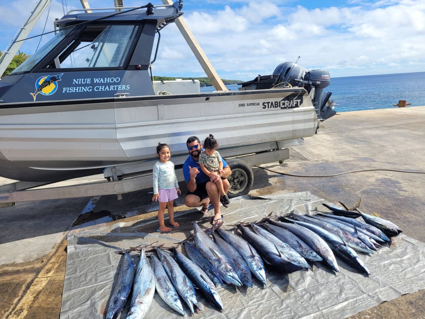father and small children in front of fishing boat with fish