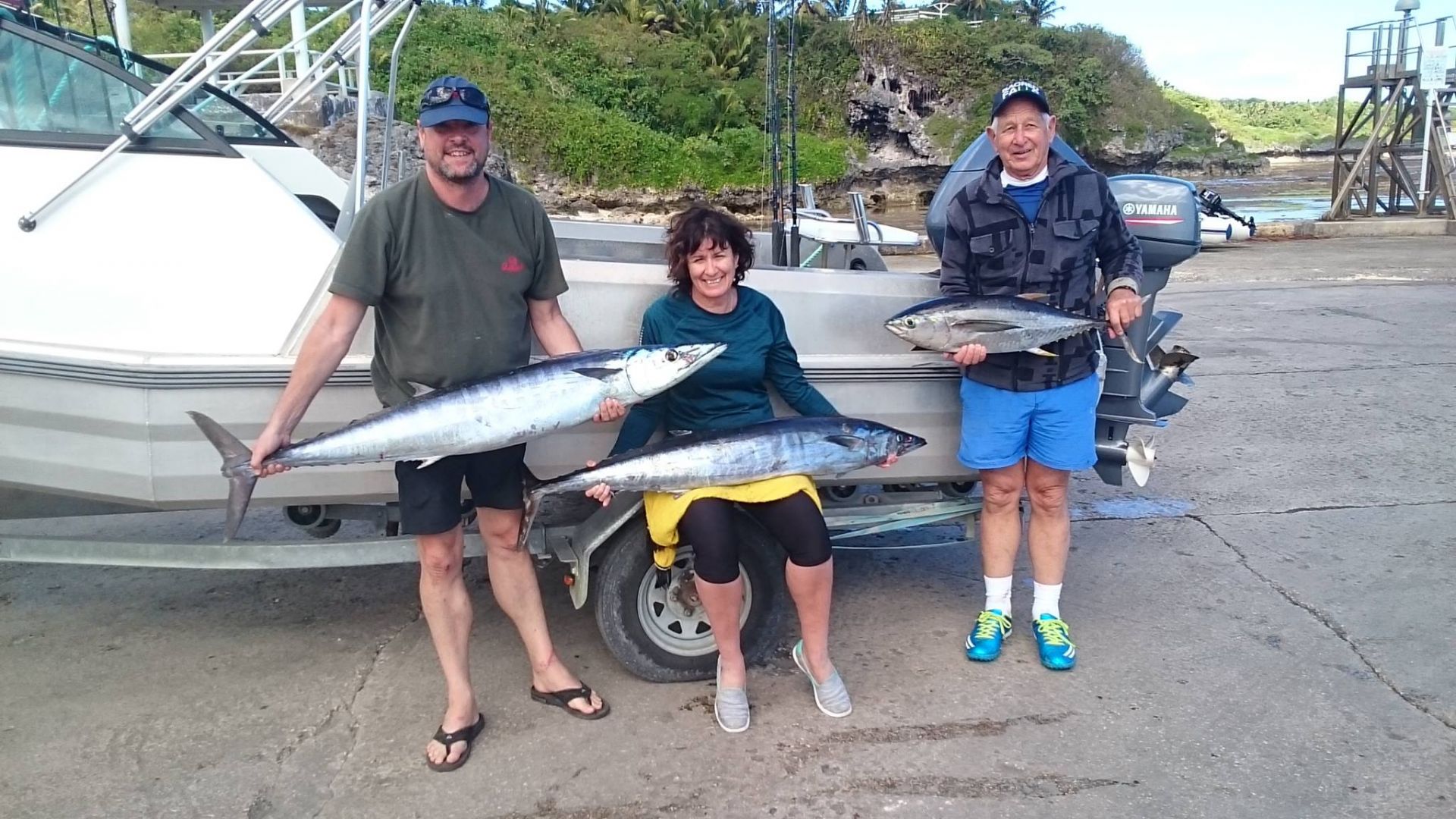 3 people in front of boat holding fish