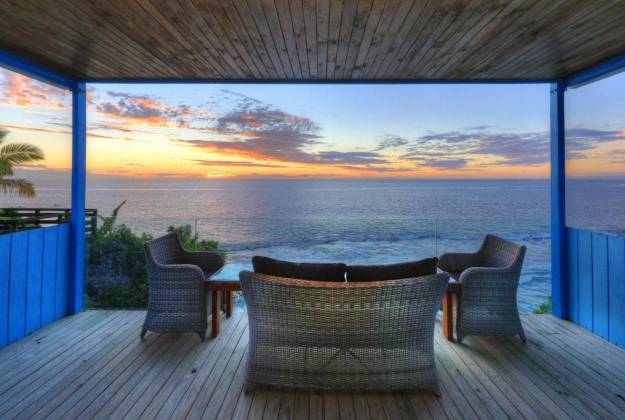 a deck with chairs and a table on it with a body of water in the background